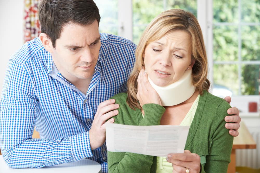 injured woman holds neck and looks at medical bill with husband