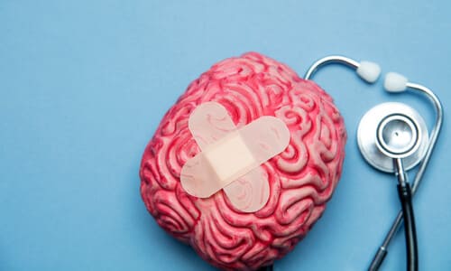 A top-down shot of a toy brain with crossed bandages on it, next to a stethoscope and against a cyan background.