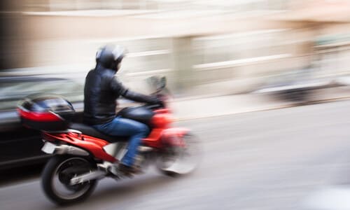A motion-blurred image of a red motorcycle speeding along a road alongside another vehicle.