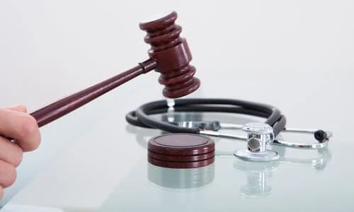 A judge's gavel striking a sound block next to a stethoscope, against a white background.