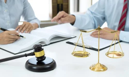 A chest-level shot of a client seeking counself from a lawyer at his desk, with a gavel and scale in the foreground.