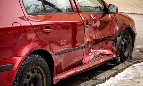 A red hatchback with a caved-in passenger-side door after a side impact.
