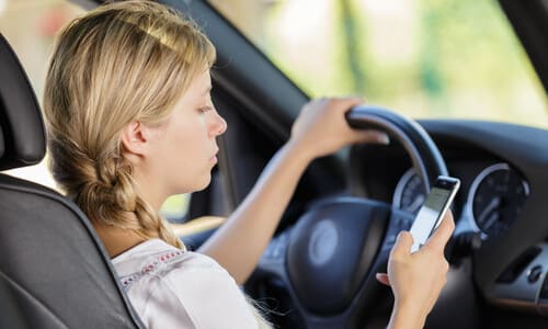 A driver texting and staring at her phone while driving on a suburban road.