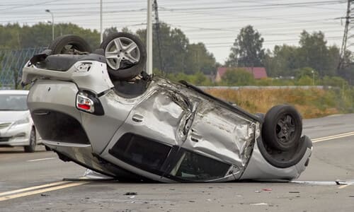 An upside-down silver hatchback after a rollover accident on the road.