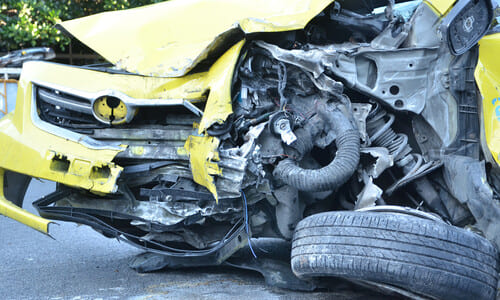 A yellow car with a damaged engine block after a collision while going the wrong way.