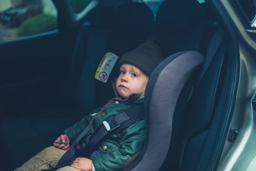 A toddler is pictured in a car seat in the backseat of a car.