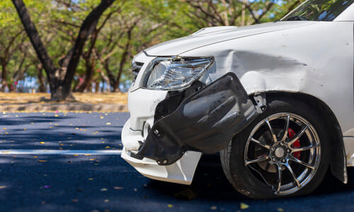 A white car with front end damage after a chain reaction car accident.