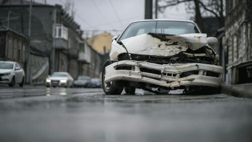 A white car with extensive front end damage after a dangerous road accident.