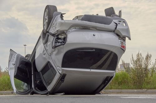 A grey sedan upside down on the highway afer losing control.