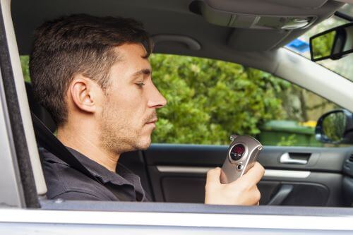 A driver looking at a breathalyzer reading after blowing into it.