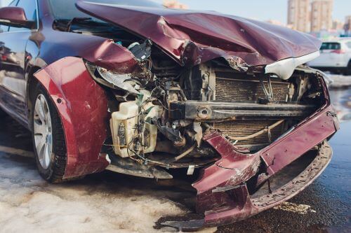 A damaged front end of a wine-red sedan after a collision during a turn.