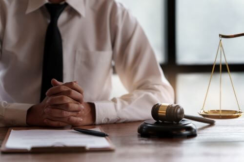 A lawyer at a desk clasping his hands together while patiently waiting for a client.