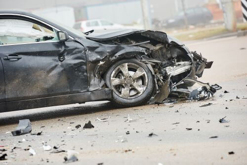 A side-view shot of a black sedan with a destroyed front end after a collision.