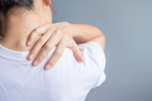 A woman in a white shirt reaching over her shoulder to nurse a back injury.