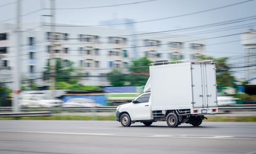 A white delivery truck speeding along a city road as it tries to make a delivery on time.