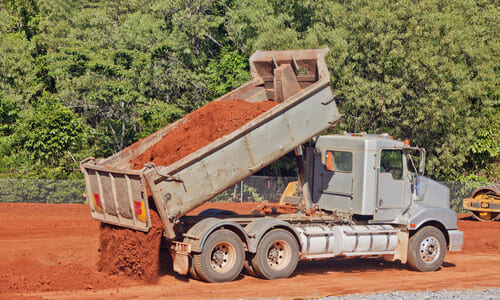 A dump truck transporting soil to a construction site and dumping its contents.