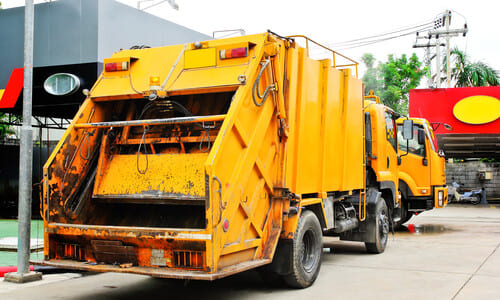 Heavy yellow garbage trucks waiting for maintenance at a garage.