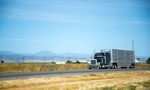 A black semi truck on an open road on a clear day with mountains in the background.
