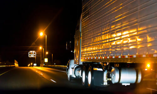 A reefer truck driving along a highway at night illuminated by streetlights.