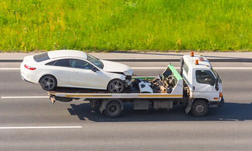 A tow truck with a white car mounted on it as it drives along a road.