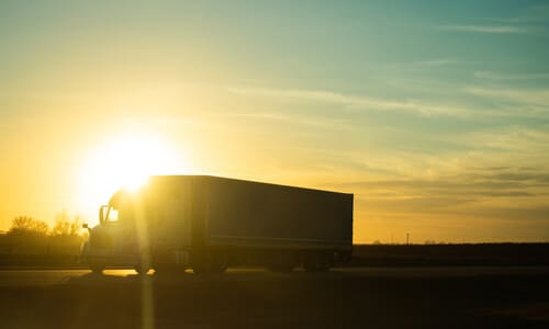 The silhouette of a truck on a highway against the late afternoon sun.