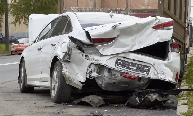 A silver car with a crushed rear-end after a car accident in a city.