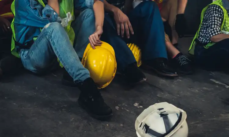 Construction workers seated next to an upturned safety helmet after a coworker was injured.