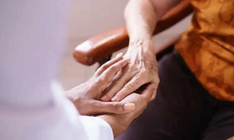 An elderly woman's hands clasped by a caretaker in a nursing home.