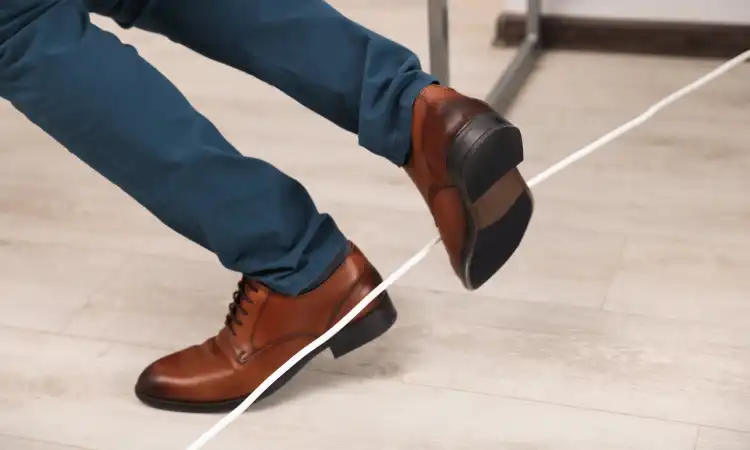 A closeup of a man's feet tripping over an unsecured power cable in an office building.