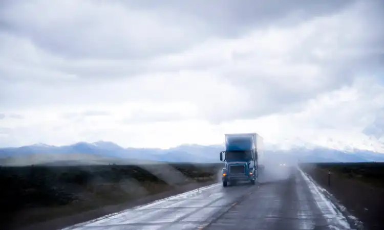 A truck on a highway on a rainy afternoon seen from the window of another vehicle.