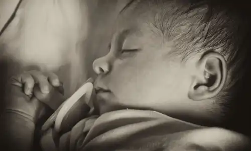 A black and white image of a newborn baby sleeping against the mother's chest.