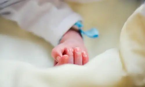 A clothed newborn's arm resting on a blanket in an incubator.