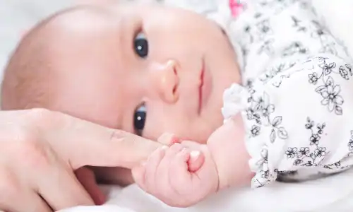 A newborn baby girl grasping the index finger of her parent's hand.