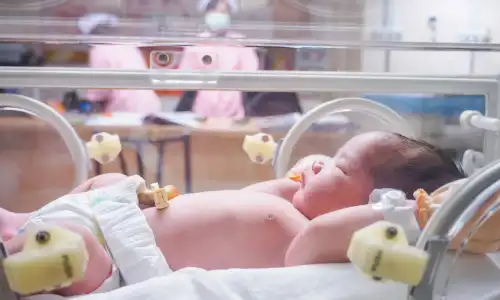 A newborn baby in an incubator with medical personnel in the background.