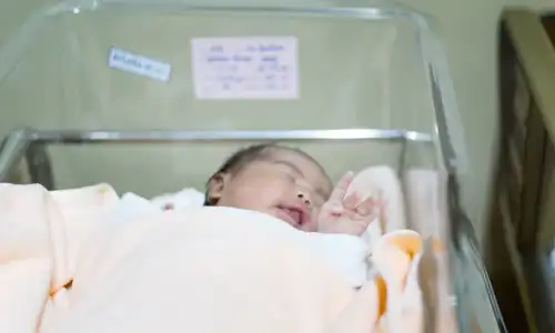 A newborn baby inside glass incubator crying for an adult.