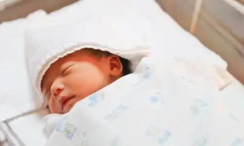 A newborn baby sleeping in an incubator wrapped in warm cloth.