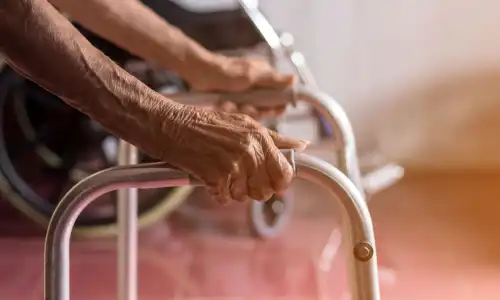 A closeup of a senior citizen in a nursing home supporting her weight by grasping a walker.