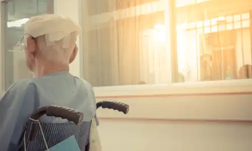 A senior citizen in a wheelchair with bandages on his head for an injury caused by a fall in a nursing home.