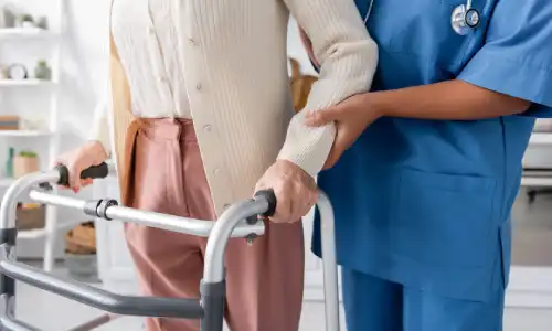 A nurse helping a senior citizen stand to see if she recovered from a nursing home fracture.