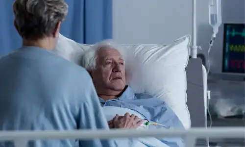 An old woman visiting her husband in a nursing home where he is suffering an infection.