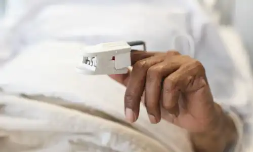 A closeup of a malnourished senior citizen's hand with a pulse oximeter clipped onto a finger.