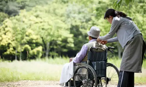 An elderly woman in a wheelchair in a garden assisted by a helper.