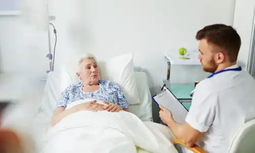 A senior citizen in bed complaining to an attending physician about pain from pressure ulcers on her back.