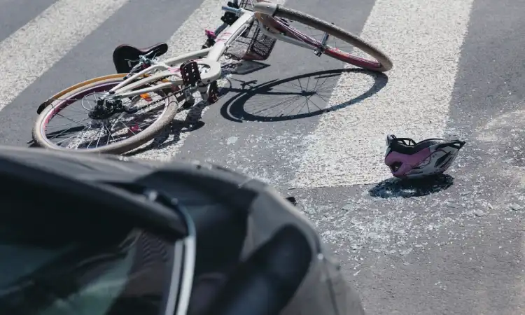 A bicycle on its side next to an upturned helmet after a collision with a car on a crosswalk.