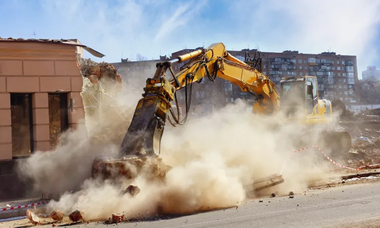 An excavator raising a cloud of dust as it works in a hazardous construction area.