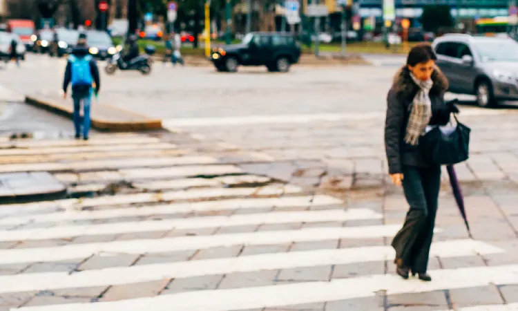 Pedestrians on a crosswalk making it across a cobblestone road in the middle of the day.