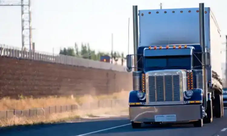 A truck driving down a major highway next to a large fence.