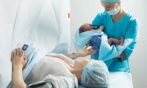 A nurse in a hospital holding a newborn baby close to the mother.
