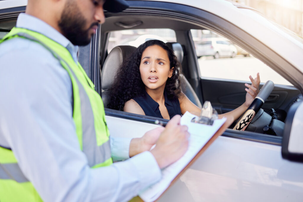 Shot of a young businesswoman looking upset at receiving a ticket from a traffic officer.