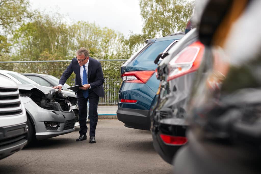 Male Insurance Loss Adjuster With Digital Tablet Inspecting Damage To Car From Motor Accident